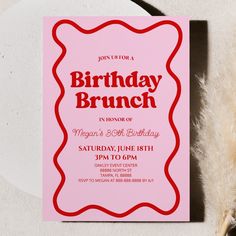 a pink birthday party card sitting on top of a white table next to a feather