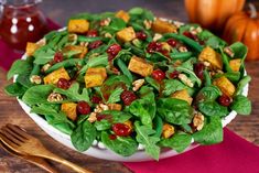 a salad with spinach, cranberries and walnuts in a white bowl