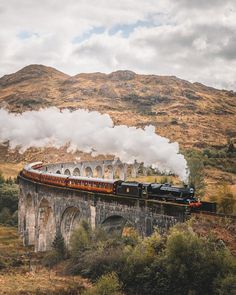 a train traveling over a bridge with steam pouring out of it