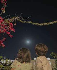 two children are looking at the moon in the night sky with pink flowers hanging over them