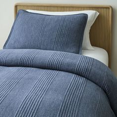 a bed with blue bedspread and pillows on top of the headboard next to a night stand