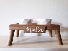 two white bowls sitting on top of a wooden stand with the word nala written in cursive letters