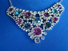 This is a very pretty vintage silver bib necklace with colourful CZ stones. It measures 18 inches in total and has an extender chain of 3 inches. The jewel encrusted bib measures 4 inches across and 2 inches from top to bottom. The vey colourful 'bib' is encrusted with sparkling imitation diamonds and sparkling CZ amethysts, sapphires and rubies. Each colourful stone lies at the centre of a  flower design of 'diamonds'. This is a spectacular and now rare piece of costume jewellery which will look stunning against any skin tone or dark dress and is sure to bring many compliments. It sparkles gloriously and spectacularly in both sunshine and artificial light and would glitter wonderfully in candlelight ! Whenever and however you choose to wear this delightful necklace, it is sure yo be a top Multicolor Crystal Rhinestone Necklace, Multicolor Crystal Rhinestone Costume Necklace, Multicolor Rhinestone Necklace With Jewels, Costume Jewelry, Multicolor Party Necklaces With 17 Jewels, Multicolor Rhinestone Necklace Costume Jewelry, Multicolor Rhinestone Wedding Necklaces, Multicolor Rhinestone Necklaces For Weddings, Silver Multi-stone Necklace For Parties, Multicolor Rhinestones Necklace For Wedding