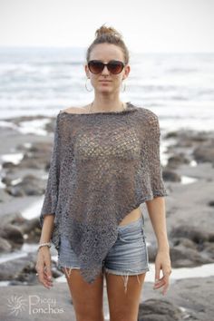 a woman standing on top of a rocky beach next to the ocean with her hands in her pockets