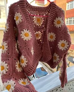 a pink sweater with white and yellow flowers is hanging on a clothes line outside in front of a building