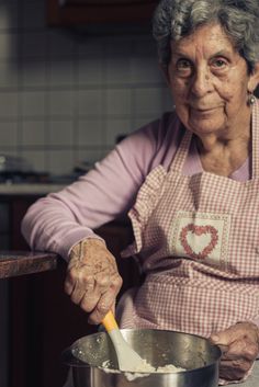 an old woman is stirring something in a pot on the stove top with a ladle