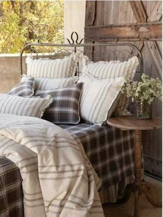 a bed with plaid sheets and pillows on top of it, next to a wooden headboard