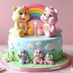 two teddy bears on top of a cake with a rainbow in the background and a lit candle