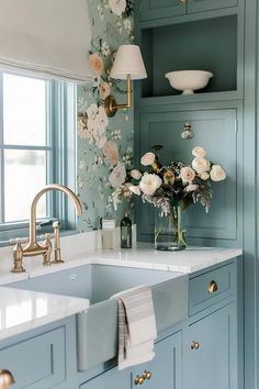 a kitchen with blue cabinets and white flowers on the wall above the sink is a gold faucet