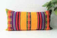 an orange and green striped pillow sitting on top of a white table next to a potted plant