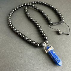 * This stunning pendant necklace features an 8mm Matte Black Onyx and black tourmaline stone with a Lapis Lazuli point. The combination of these stones creates a powerful and stylish accessory for men. * The necklace is adjustable, allowing for a perfect fit for any neck size ending with 6mm hematite beads.  The matte black finish of the Onyx and tourmaline stones adds a sleek and modern touch to the design. * The Lapis Lazuli point adds a pop of color and a touch of elegance to the overall look Obsidian Necklace With 8mm Beads As Gift, Black Gemstone Beaded Necklace, Black Gemstone Beaded Necklace For Meditation, Black Amulet Necklace With Natural Stones, Obsidian Necklace With Gemstone Beads As Gift, Obsidian Gemstone Beads Necklace As Gift, Obsidian Gemstone Beads Necklace For Gift, Black Crystal Pendant Necklace With Gemstone Beads, Black Pendant Necklace With Stones