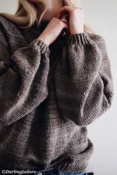 a woman wearing a sweater and jeans poses for the camera with her hand on her neck