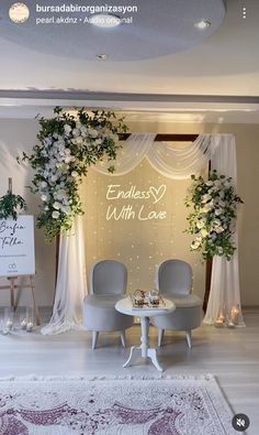 a wedding stage with two chairs and flowers on the back drop off table, surrounded by white draping