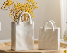 two white bags sitting on top of a wooden table next to flowers and vases