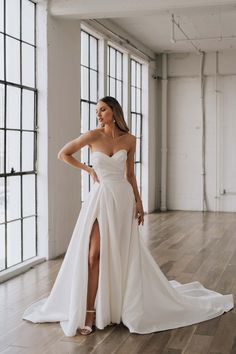 a woman in a white wedding dress standing on a wooden floor with her hands on her hips