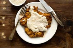 a white plate topped with fried chicken covered in gravy next to a fork