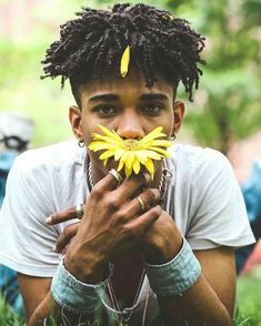 a young man with dreadlocks holding flowers in front of his face