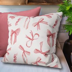 a white pillow with pink bows on it next to a potted plant and other decorative items