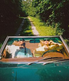 two people sitting in the back seat of a convertible car on a dirt road surrounded by trees