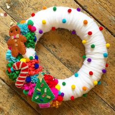 a white wreath decorated with colorful pom - poms on top of a wooden floor