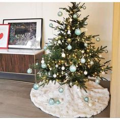 a small christmas tree with blue and white ornaments on it's base in a living room