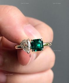 a person is holding an emerald and diamond engagement ring in their left hand, with the other two diamonds on each side