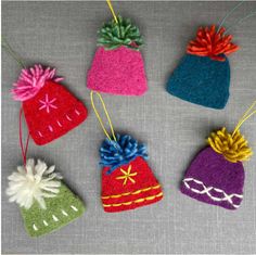 four knitted hats hanging from strings on a gray surface, each with different colors