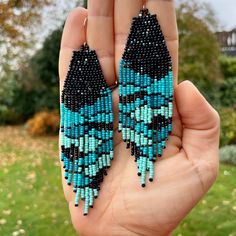 a person holding up two pairs of beaded earrings in front of some grass and trees