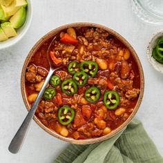 a bowl filled with chili and meat next to other food on a table, including avocado