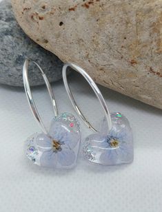 These exquisite handcrafted earrings feature real dried flowers, delicately preserved in clear resin. Each pair is truly one-of-a-kind, showcasing a unique blend of blue flowers and silver leaf, suspended on solid 925 sterling silver hoops. Details: Hoop Material: 925 Sterling Silver Hoop Size: 24mm Flower Setting: Clear Resin Please note that due to the natural variation of each flower, your earrings may differ slightly from the images shown, adding to their individual charm. For any additional Silver Drop Earrings With Pressed Flowers, Silver Pressed Flowers Drop Earrings, Silver Sterling Flower Earrings With Pressed Flowers, Silver Sterling Silver Earrings With Pressed Flowers, Silver Pressed Flower Earrings In Resin, Silver Resin Earrings With Pressed Flowers, Silver Pressed Flower Resin Earrings, Silver Round Earrings With Pressed Flowers, Handmade Silver Resin Flower Earrings