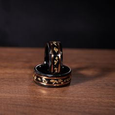 two wedding rings sitting on top of each other in front of a black background with gold flowers