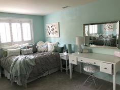 a bed room with a neatly made bed and a desk in front of a mirror