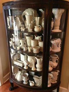 a display case filled with white vases on top of a hard wood floor next to a wall