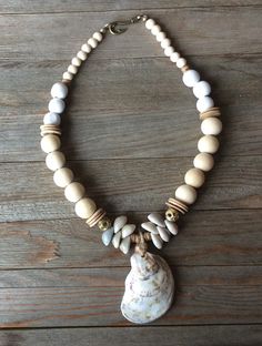 This freshwater oyster is flanked on both sides by Cowrie shells, coconut wood beads, polished natural wood beads and distressed white wood beads.  The fish hook clasp makes for a fun back view!  The neutral colors look like a walk on the shore and go with every summer outfit.  It will be your favorite accessory! Cheap Shell Necklaces With Round Beads, Cheap Handmade Shell Necklace, White Cowrie Shell Necklace In Beachy Style, White Cowrie Shell Necklace With Beachy Style, Handmade White Ocean-inspired Beaded Necklace, White Cowrie Shell Beachy Necklace, Beachy White Cowrie Shell Necklace, White Wooden Beaded Necklaces For Beach, White Shell Beaded Necklaces In Beachy Style