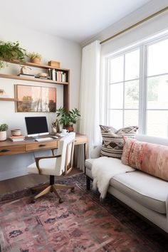 a white couch sitting in front of a window next to a wooden desk with a laptop computer on top of it