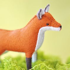 an orange fox figurine is standing in the mossy ground with its tail curled up