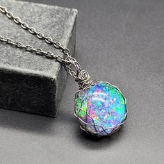 Embrace the mystery of the universe with this round galaxy cabochon set in braided darkened steel! It is totally handmade, with unique original design. The double sided pendant features amazing iridescent sparkling colors that opalesce and bot refracts and light to show a rainbow nebula on one side and a black backed cabochon.  It is made with heat darkened steel, using man-made cabochons instead of mined gems, so it is very environmentally friendly. Handmade Iridescent Metal Jewelry, Unique Iridescent Round Jewelry, Handmade Iridescent Round Jewelry, Unique Stainless Steel Round Pendant Jewelry, Unique Stainless Steel Round Pendant, Mystical Round Cabochon Jewelry, Iridescent Opal Round Jewelry, Iridescent Round Opal Jewelry, Iridescent Opal Jewelry