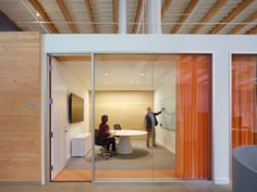 two people are standing in an office with glass walls and sliding doors to the outside