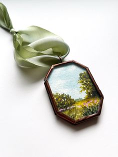 an ornament with a green ribbon hanging from it's side on a white surface