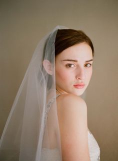 a woman in a wedding dress with a veil on her head looking at the camera