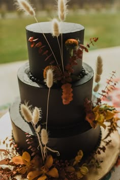 a three tiered cake decorated with feathers and dried flowers on a table in front of a grassy area