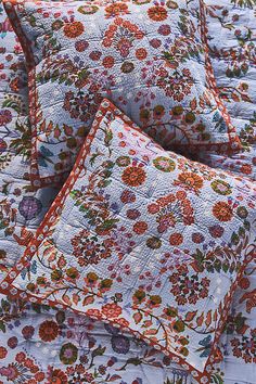 four pillows are stacked on top of each other in front of a bed with an orange and white floral pattern