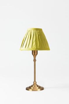 a gold lamp with a yellow shade on it's base and a white wall in the background