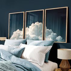 a bedroom with blue walls and white linens on the bed, two paintings above the headboard