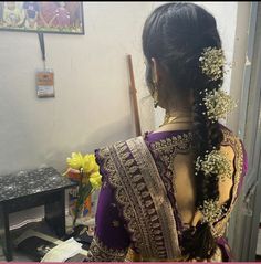 a woman with braids and flowers in her hair is looking into the mirror while wearing a sari