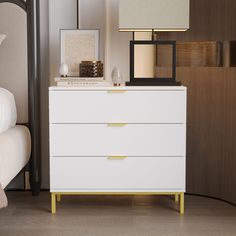 a white dresser sitting next to a bed with a lamp and pictures on top of it