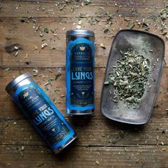 two cans of linds on a wooden table next to a metal tray with dried herbs