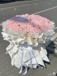 a large bouquet of pink roses is wrapped in white paper on the side of the road