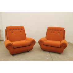 two orange chairs sitting next to each other in a room with white walls and concrete flooring