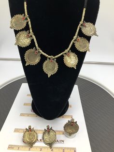 This complete vintage coin set includes a necklace, a pair of earrings, and a ring, is an epitome of tradition, as the design of the set is inspired by the Afghani Kuchi ornaments. The rusty gold toned set is embellished with dangling elements, adorned with intricate patterns and archaic motifs. The pair of earrings, coin shaped, complete the set in an astonishing manner, complimented by the antique ring in the identical design. You can pair this complete traditional set with any traditional or Brass Coin Pendant Jewelry, Vintage Medallion Jewelry For Festival, Vintage Medallion Jewelry For Festivals, Vintage Festival Medallion Jewelry, Antique Handmade Coin Necklace For Festival, Gold Brass Coin Pendant Jewelry, Gold Coin Pendant Brass Jewelry, Vintage Gold Jewelry With Coin Pendant, Handmade Antique Coin Necklace For Festival